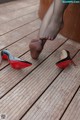 A woman in black stockings and red high heels on a wooden deck.