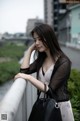 A woman leaning on a railing with a handbag.