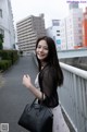 A woman standing on a bridge holding a black bag.