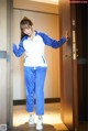 A woman in a blue and white track suit standing in front of a door.