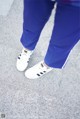 A person wearing blue pants and white sneakers on a sidewalk.