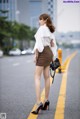 A woman in a white blouse and brown skirt is standing on the street.