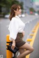 A woman in a white shirt and brown skirt leaning against a yellow pole.