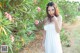 A woman in a white dress standing in front of a bush.