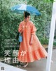 A woman in an orange dress holding an umbrella.