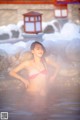 A woman in a pink bikini sitting in a hot spring.