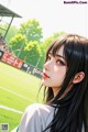 A girl with long black hair standing in front of a soccer field.