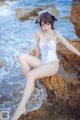 A woman in a white bathing suit sitting on a rock by the ocean.