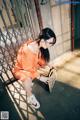 A woman in an orange jumpsuit crouching down with a suitcase.